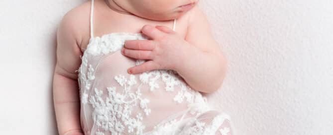 a newborn sleeping in a lace romper suit