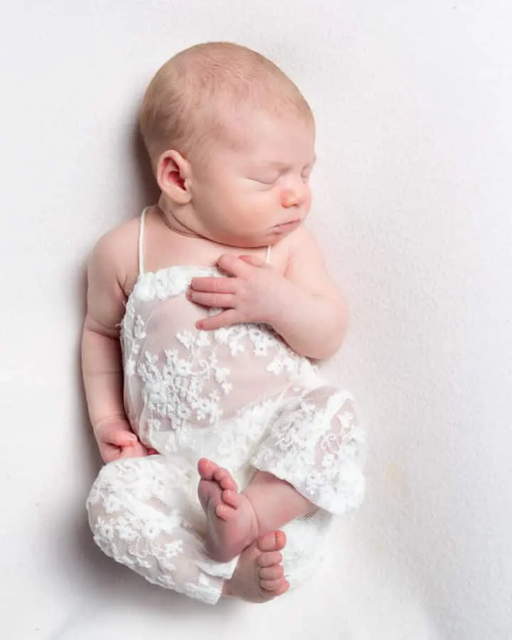 a newborn sleeping in a lace romper suit