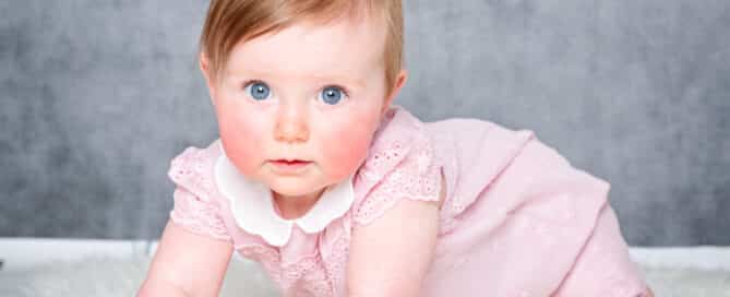 a little girl in a pink romper crawls against a grey fine art background