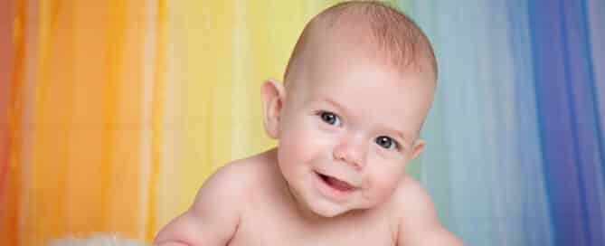a baby poses on their tummy against a rainbow curtain on a fluffy blanket