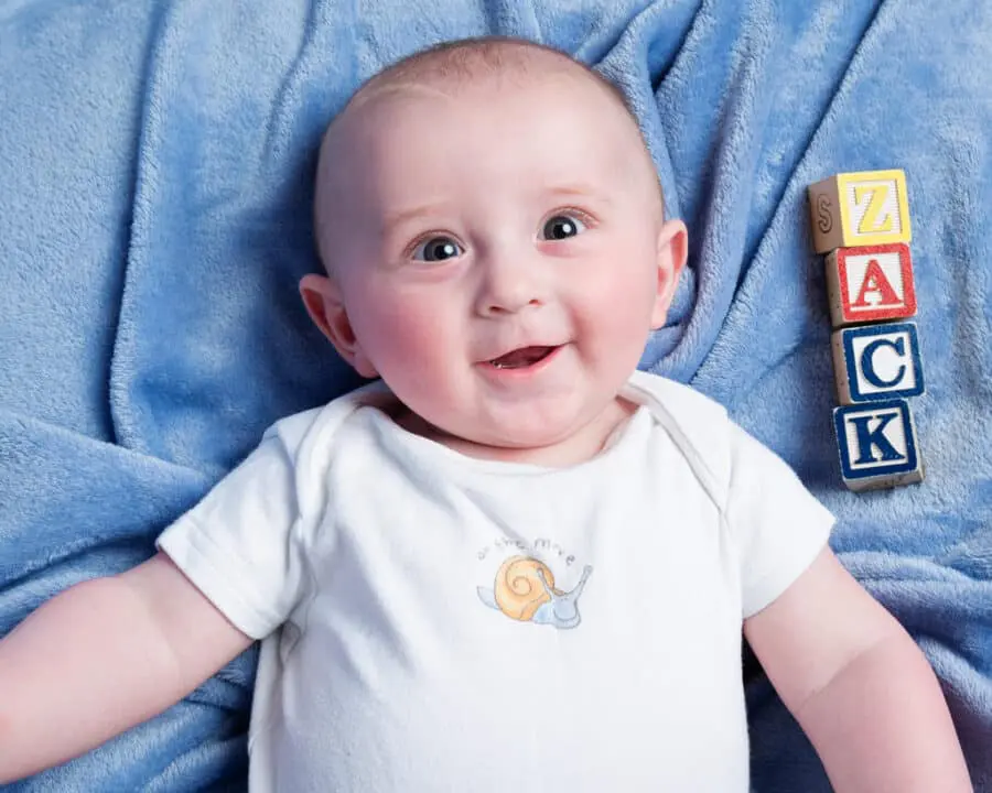 a little boy looking upat the camera with his name spelled out in letter blocks beside him