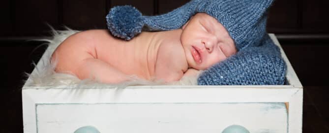 a little boy sleeping in a prop drawer with a blue hat on