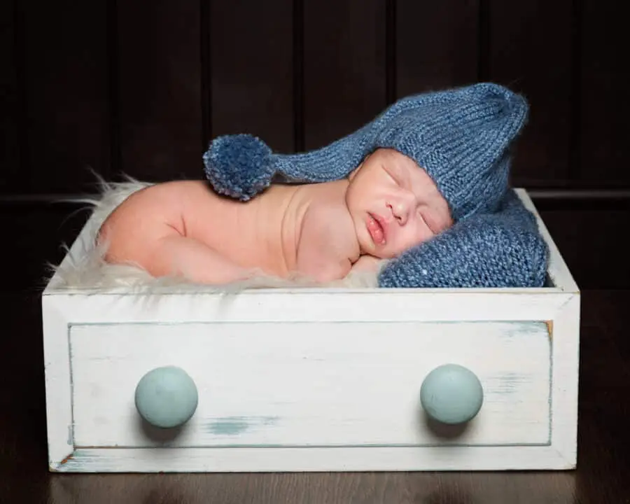 a little boy sleeping in a prop drawer with a blue hat on