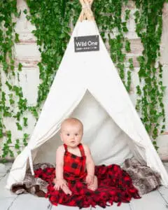 Baby Photography East Grinstead West Sussex a baby in a red plaid romper poses in a miniature teepee