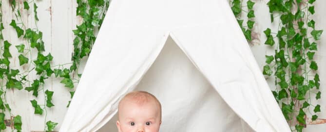 a baby in a red plaid romper poses in a miniature teepee