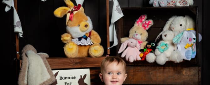 a baby posing in front of a 'shop' with all of her toy bunnies