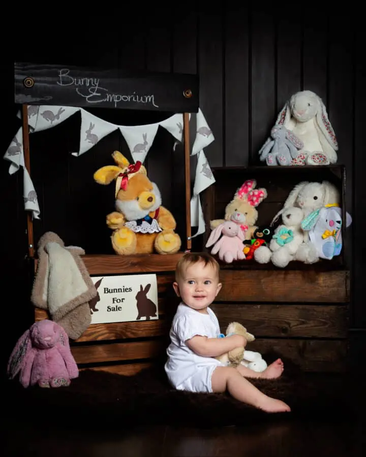 a baby posing in front of a 'shop' with all of her toy bunnies