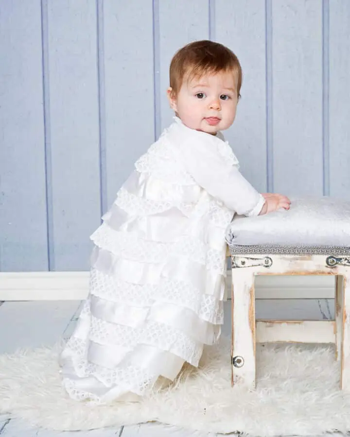 Baby Photography East Grinstead West Sussex a baby poses in a white christening gown in front of a blue backdrop