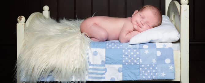 a little boy sleeps on his tummy on a mini white bed