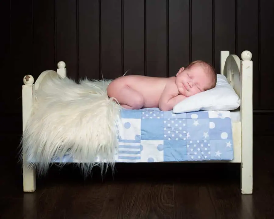 a little boy sleeps on his tummy on a mini white bed