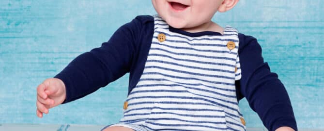 a baby posing in front of a blue canvas and laughing for the camera