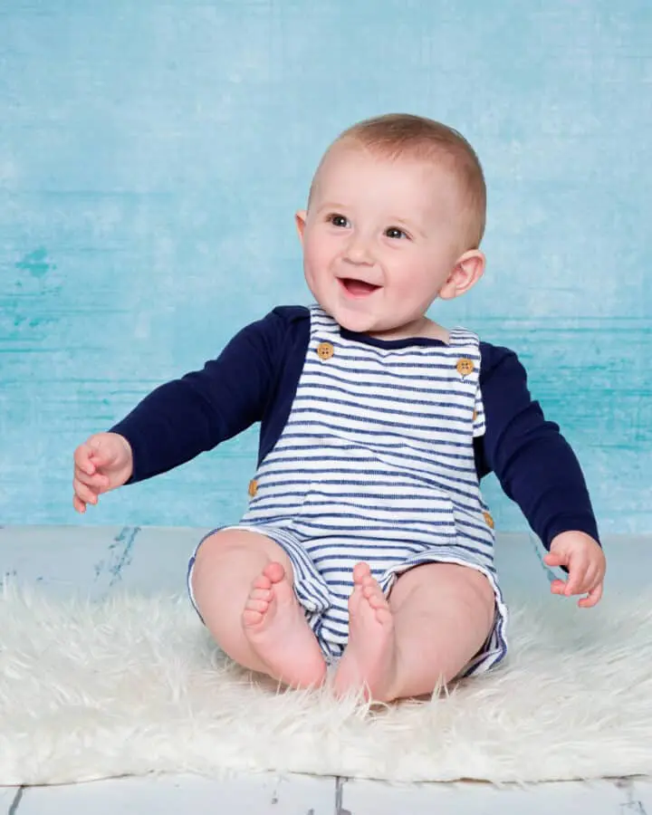 a baby posing in front of a blue canvas and laughing for the camera