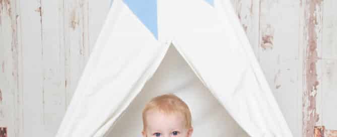 a little boy sits in a blue and white themed teepee tent