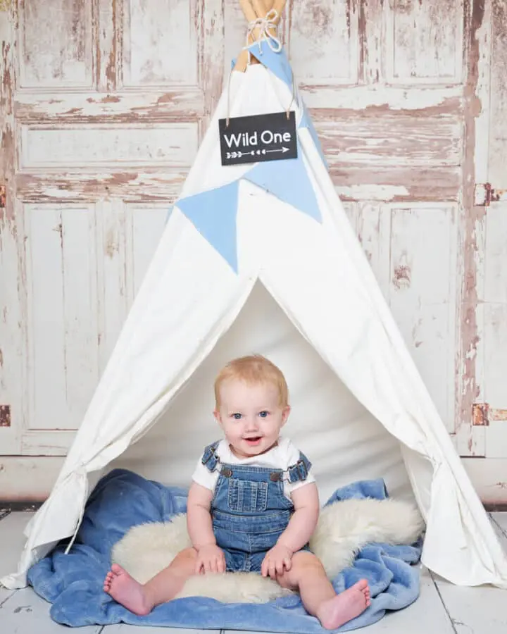 a little boy sits in a blue and white themed teepee tent