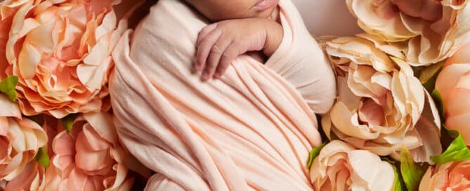 a sleeping newborn with a peach headband snoozing in a bed of peach peonies