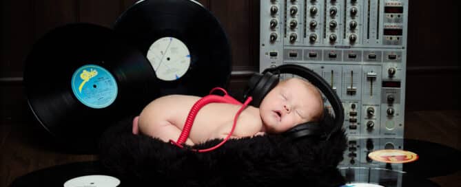 A newborn baby sleeps wearing headphones in front of a mixing deck and surrounded by records