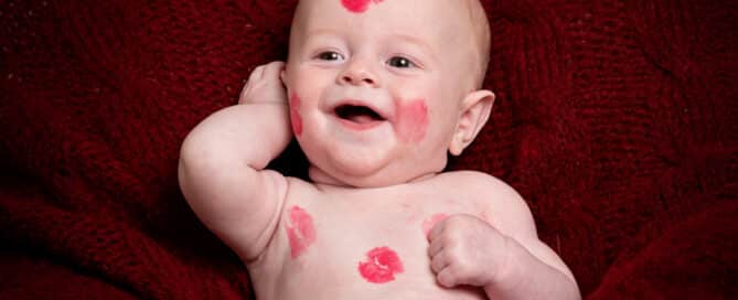a little boy covered in lipstick kiss marks against a deep red blanket