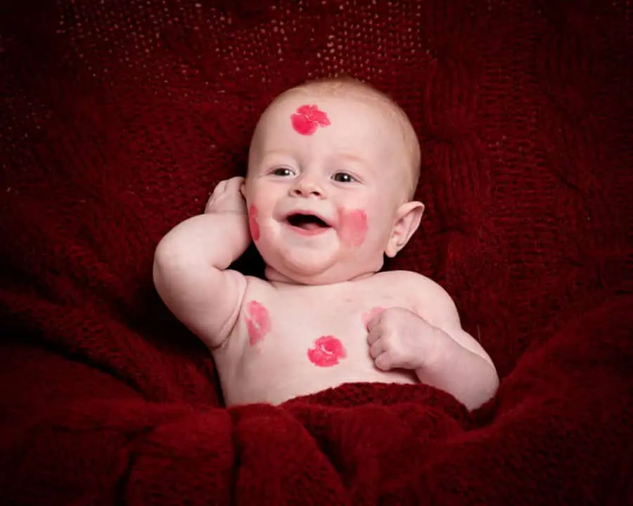 a little boy covered in lipstick kiss marks against a deep red blanket