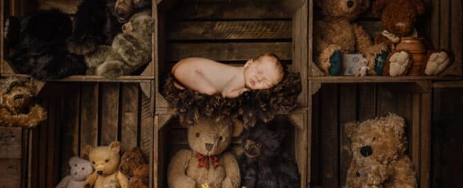 a digital image of a newborn sleeping among crates of teddy bears