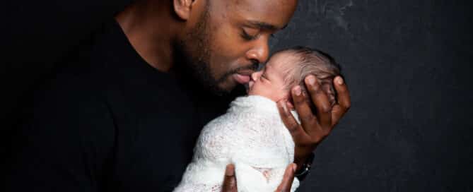 a dad kisses his newborn against a dark background