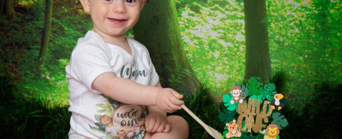 a little boy with a bright green cake sits in front of a woodland backdrop