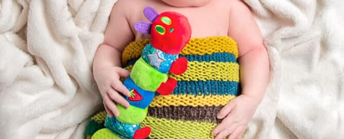 a newborn dressed in a hungry caterpillar outfit and holding a caterpillar toy