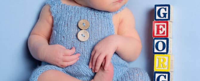 a newborn in dungarees sleeps next to blocks spelling out his name