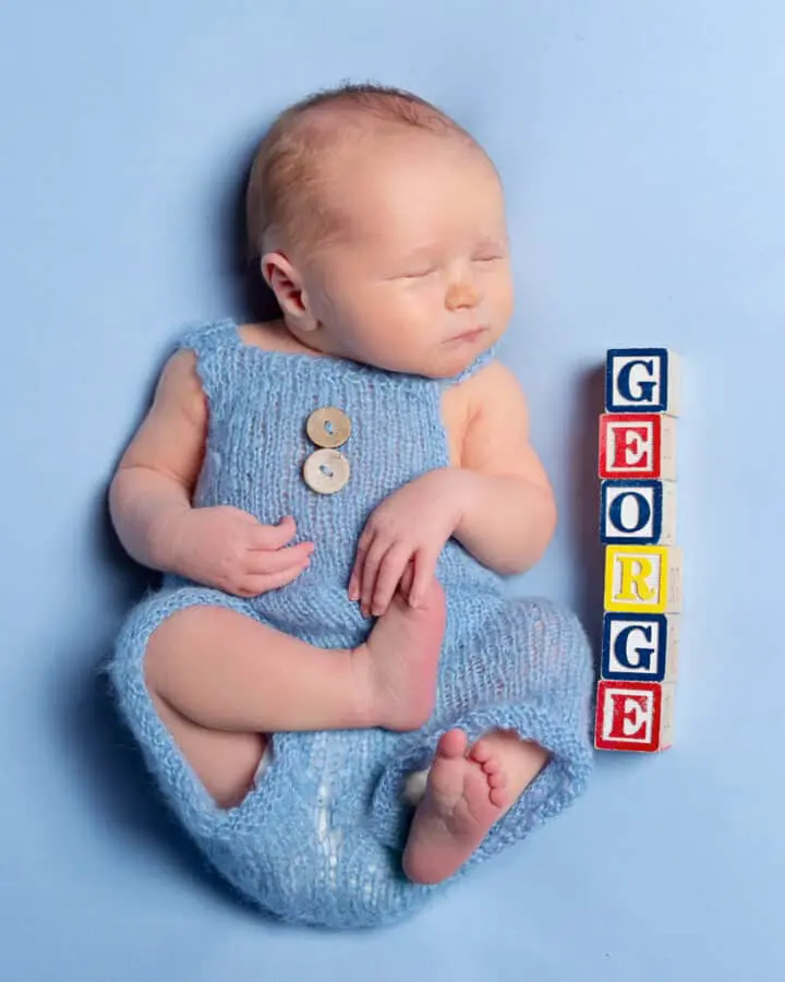 a newborn in dungarees sleeps next to blocks spelling out his name