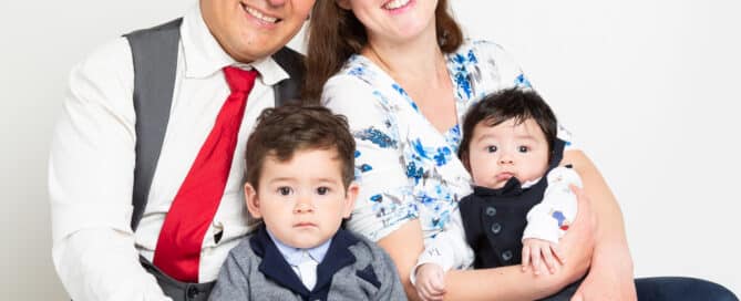a mum and dad pose with their older son and newborn baby