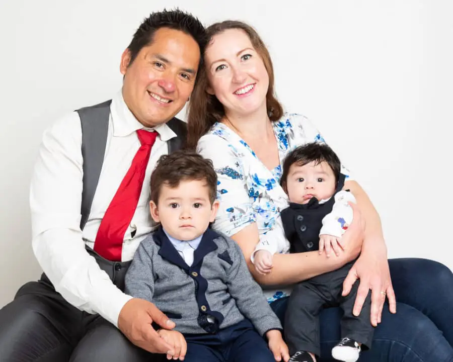 a mum and dad pose with their older son and newborn baby