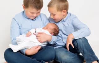 two older brothers dressed in blue hold their newborn sibling