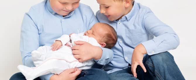 two older brothers dressed in blue hold their newborn sibling