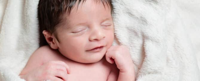 a newborn smiling in their sleep wrapped in a cream blanket