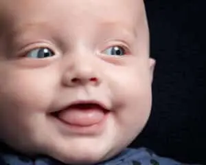 a close up of a smiling baby against a dark background in my studio