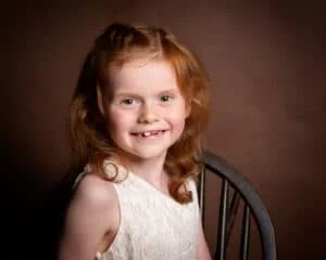 Family Portrait Photo Shoot East Grinstead West Sussex a little girl with red hair poses for a photo against a brown background