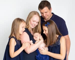 Family Portrait Photo Shoot East Grinstead West Sussex A mum, dad, two older daughters and a newborn arrival pose for a family photo all dressed in navy