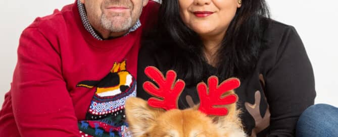 a couple pose with their corgi dog all wearing reindeer antlers