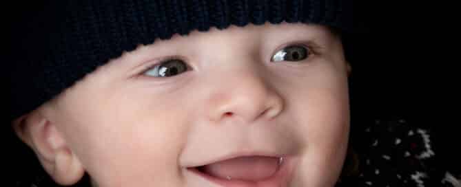 a close up of a smiling baby wearing a navy blue hat
