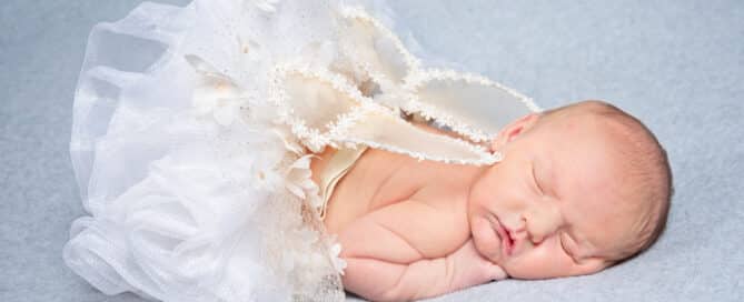 a newborn sleeps on her tummy wearing a tutu and white angel wings