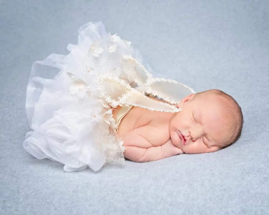 a newborn sleeps on her tummy wearing a tutu and white angel wings