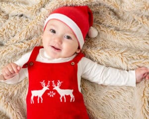 a baby on a fluffy blanket wearing a festive outfit and santa hat
