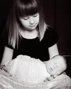 Newborn Photography East Grinstead West Sussex A little girl looks down at her sleeping baby brother on her lap - in black and white