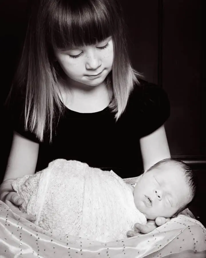 A little girl looks down at her sleeping baby brother on her lap - in black and white