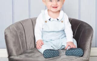 a baby in a blue romper sits on a grey mini chair