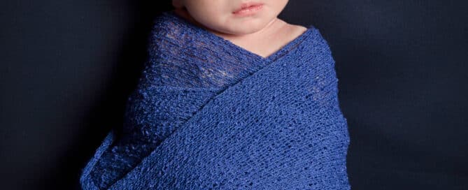 a newborn swaddled in blue on a navy blanket