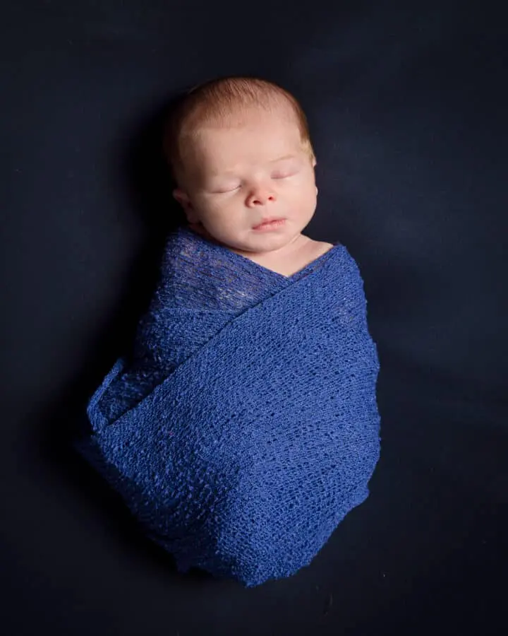 a newborn swaddled in blue on a navy blanket