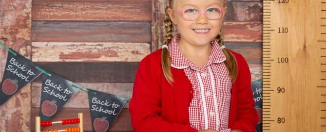 a little girl in a red school uniform poses in a studio school themed set