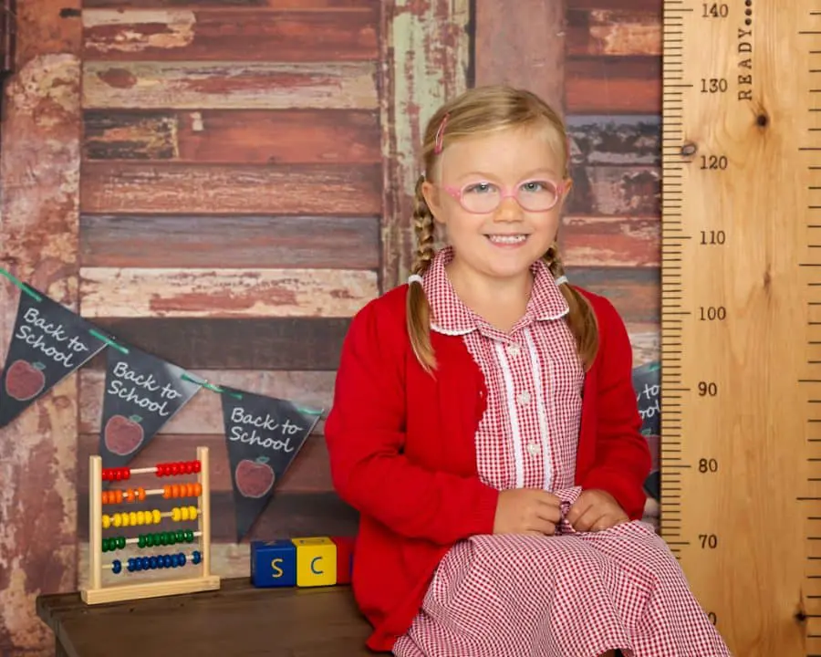 a little girl in a red school uniform poses in a studio school themed set