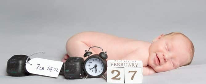 a smiling newborn lies on their front with their birth details in front of them