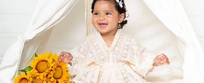 a little girl is laughing while wearing a lace outfit and sitting with some sunflowers